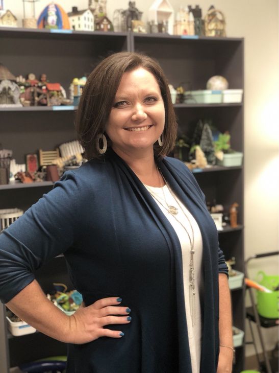 A woman in a blue cardigan is standing in front of a shelf with toys on it.