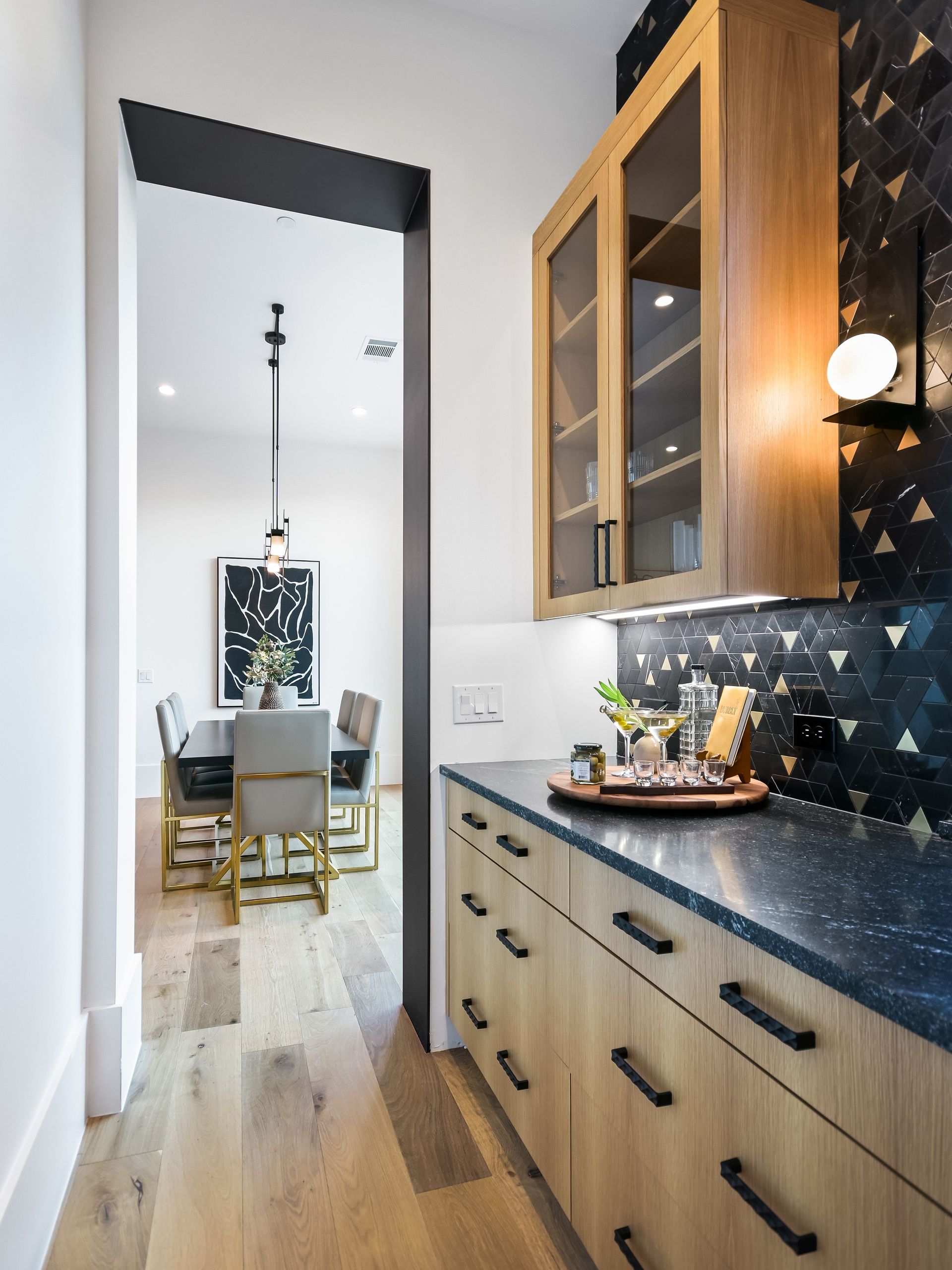 A kitchen with wooden cabinets and black counter tops leading to a dining room.
