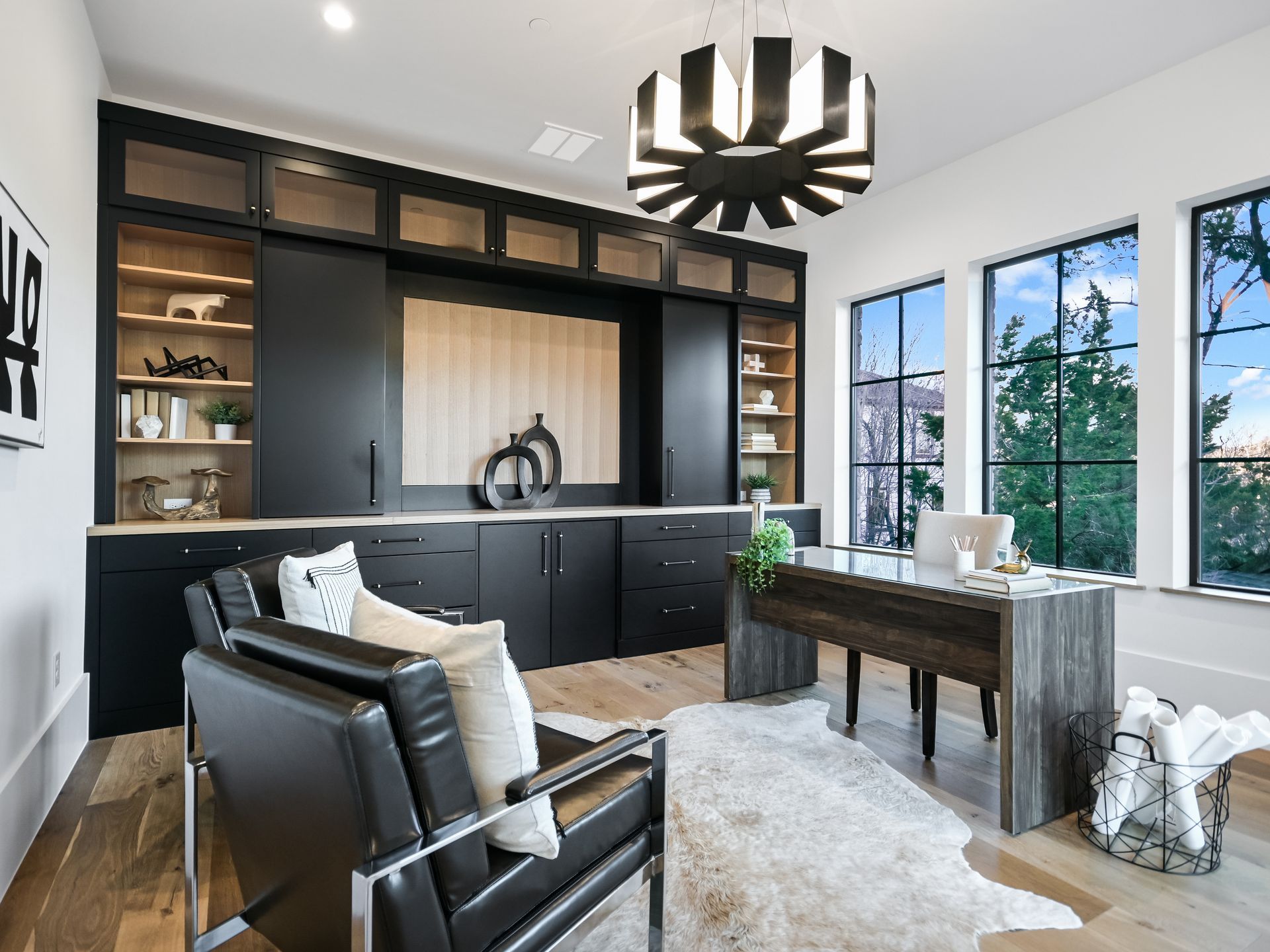 A home office with a desk , chairs , shelves and a chandelier.