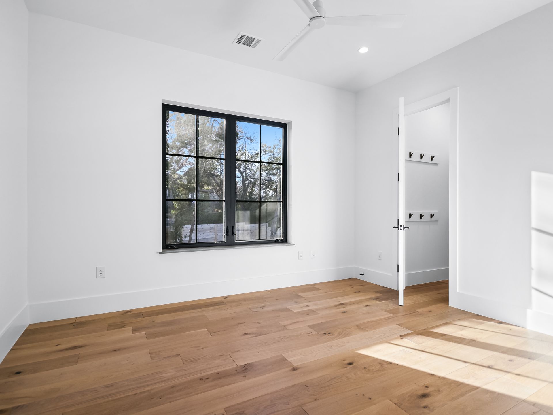 An empty bedroom with hardwood floors , a window and a ceiling fan.