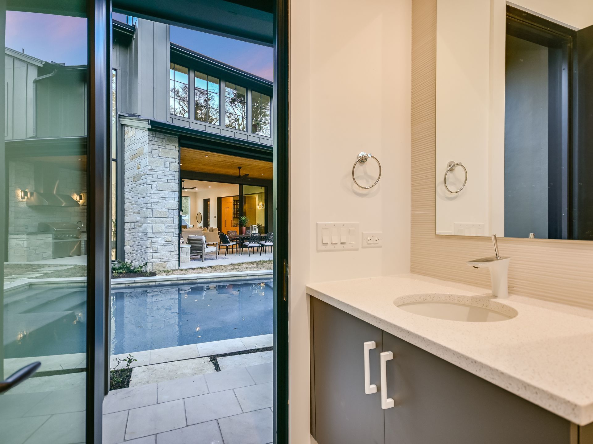 A bathroom with a sink , mirror and sliding glass door leading to a pool.