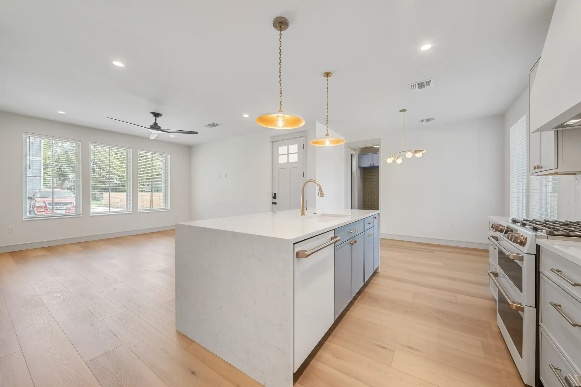 Modern kitchen with island, pendant lights, light wood floor, and stainless steel appliances.