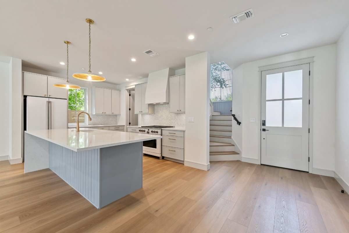 Light-filled kitchen with a large island, white cabinets, gold pendant lights, and access to outdoor stairs.