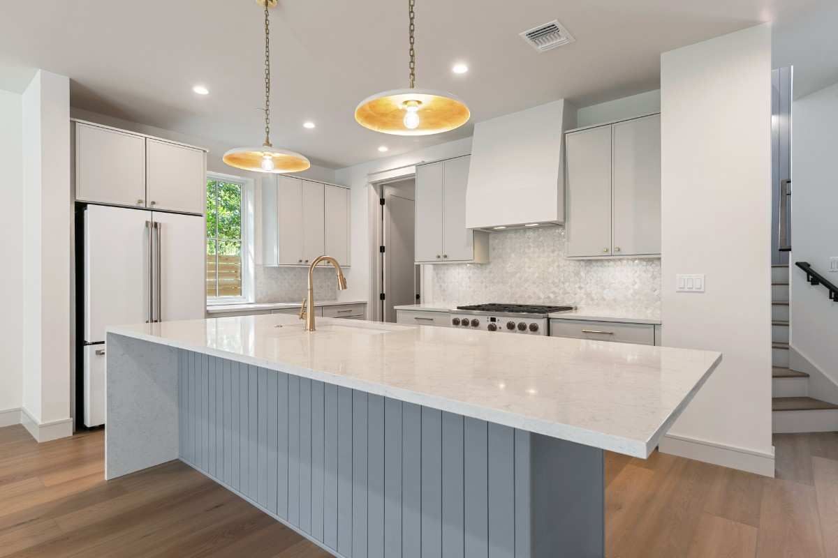 Modern white kitchen with island, gold pendant lights, and stainless steel appliances.