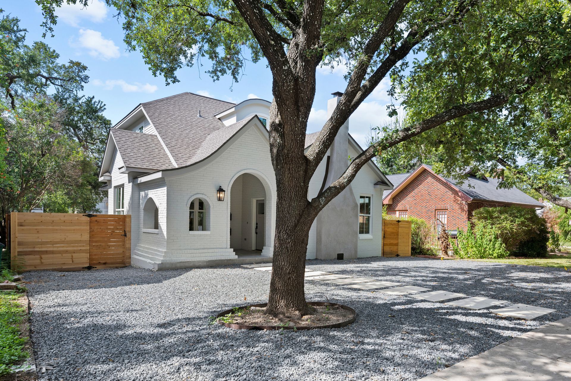 A white house with a gravel driveway and a tree in front of it