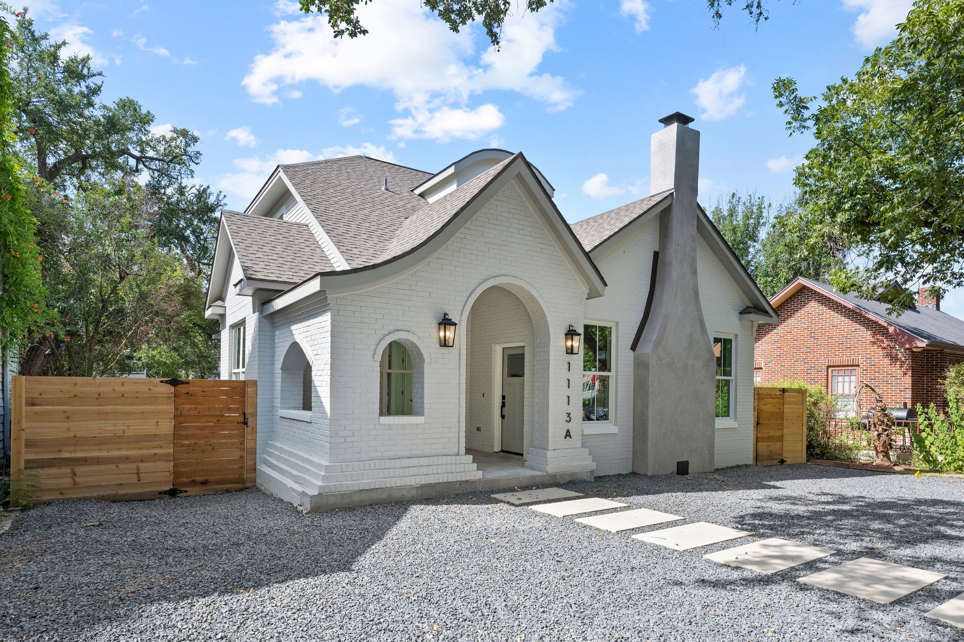 A white brick house with a gravel driveway in front of it.