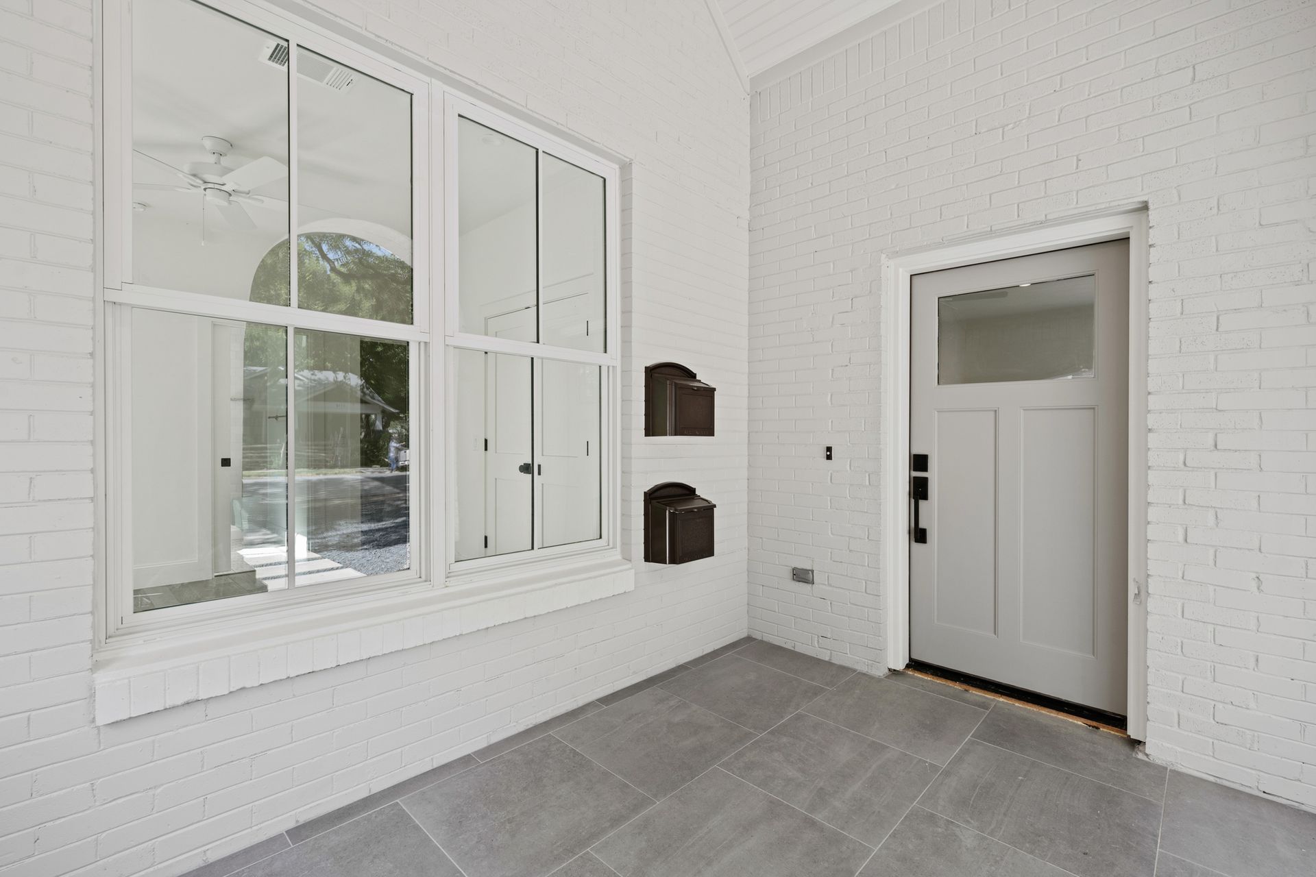 An empty porch with a white door and two windows.