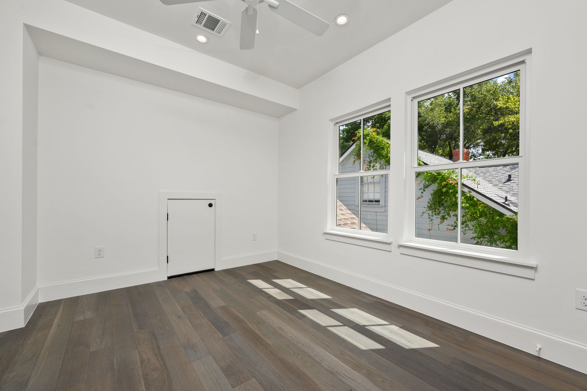 An empty room with two windows and a ceiling fan.