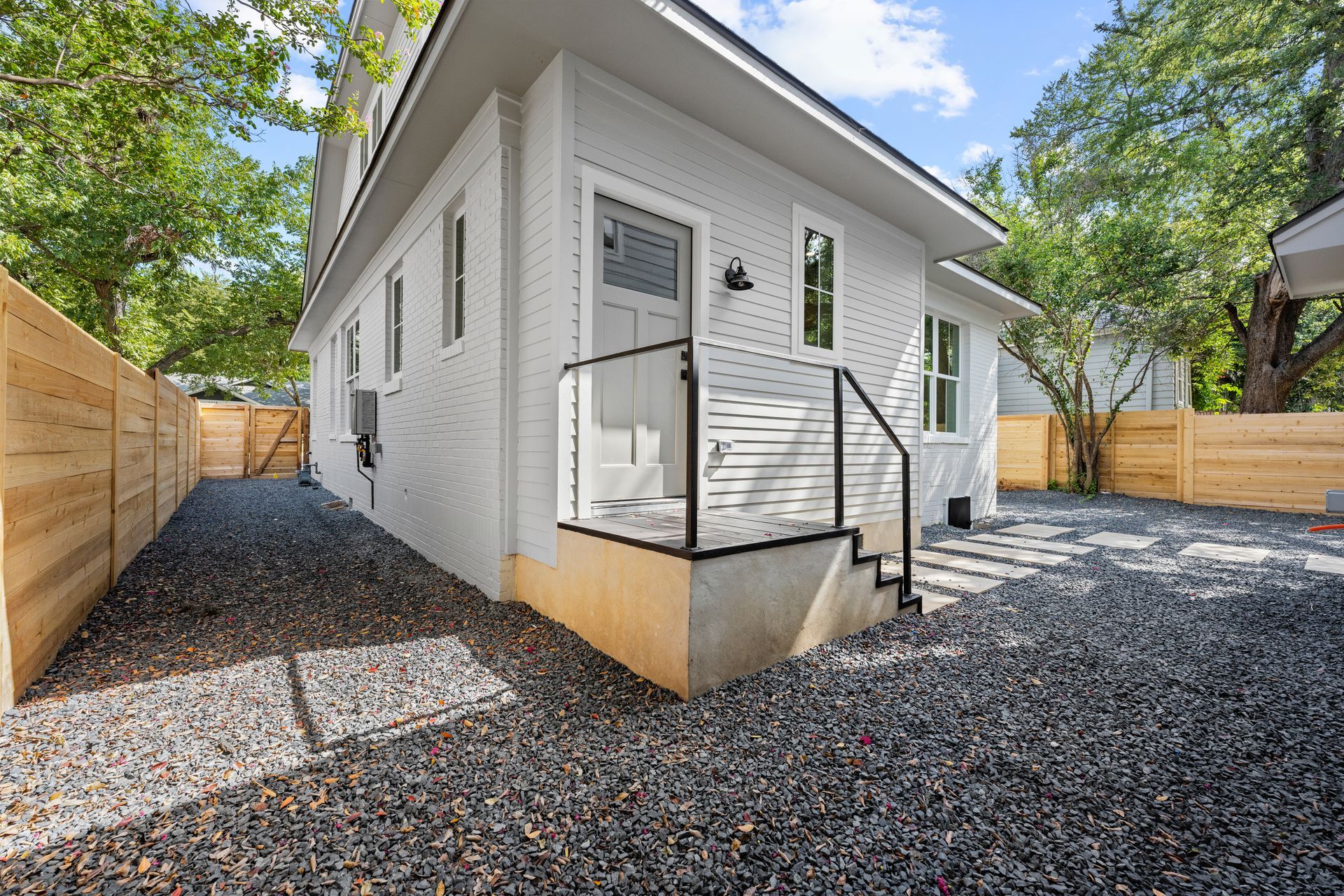 A white house with a wooden fence and gravel driveway.