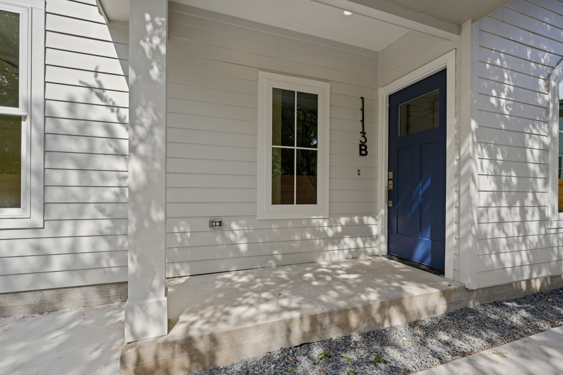 The front porch of a house with a blue door and a window.