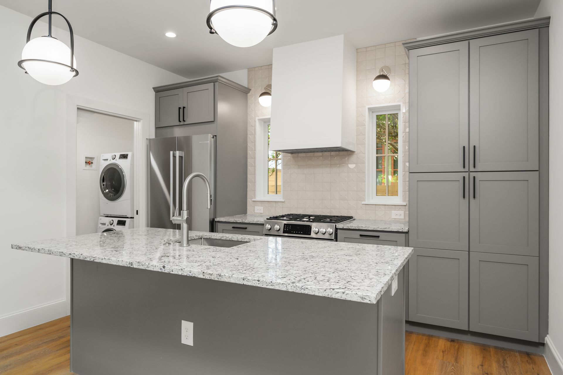 A kitchen with gray cabinets , granite counter tops , stainless steel appliances and a large island.