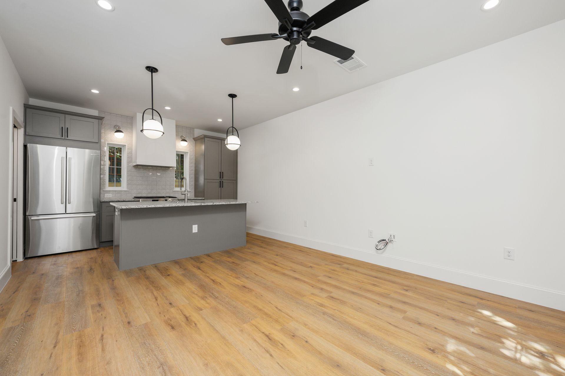 A living room with a ceiling fan and a kitchen in the background.