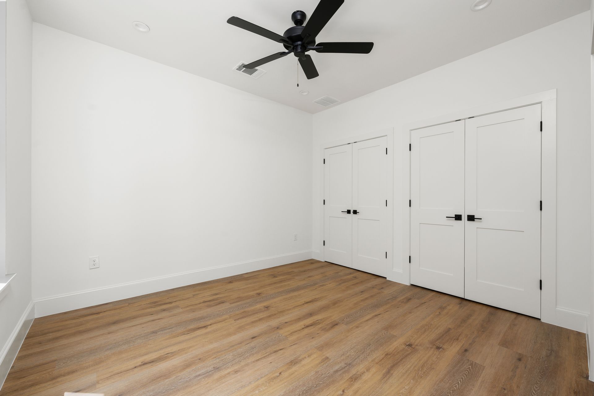 An empty bedroom with hardwood floors and a ceiling fan