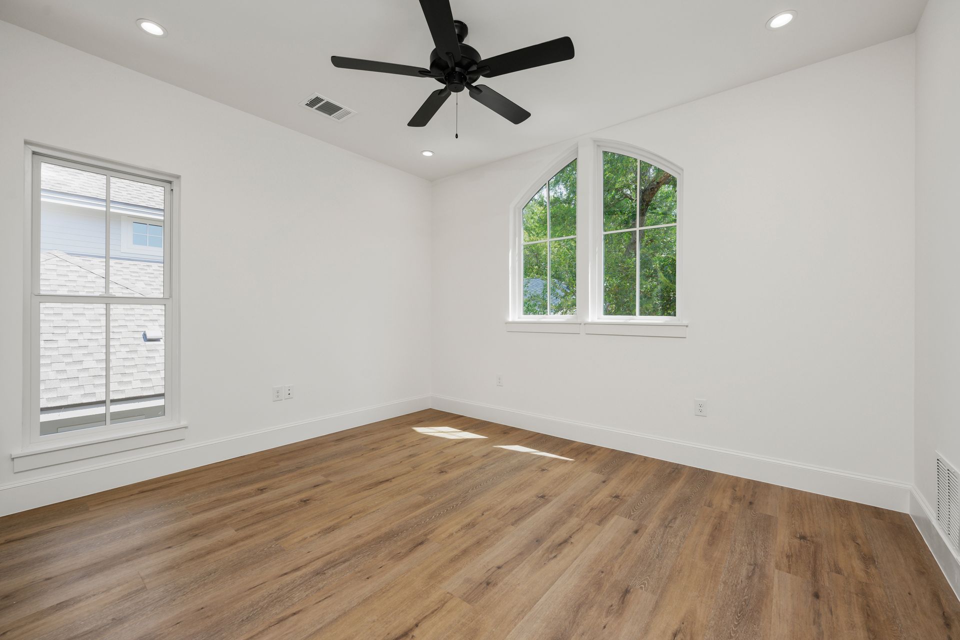 An empty bedroom with hardwood floors and a ceiling fan.