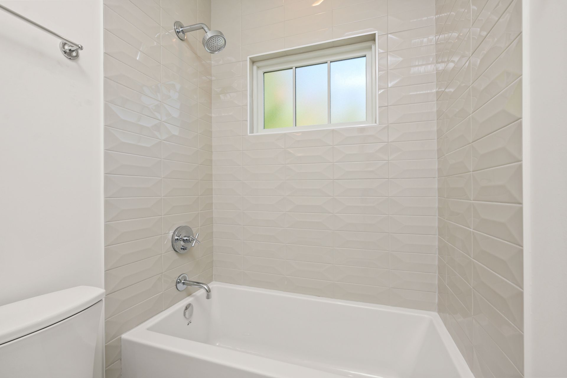 A bathroom with a tub , toilet , shower and window.