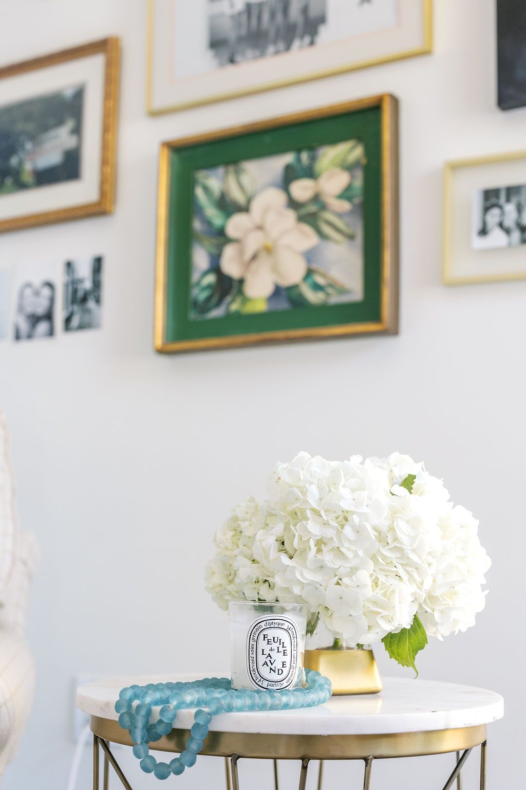 A vase of white flowers is sitting on a table in front of a wall with pictures on it.