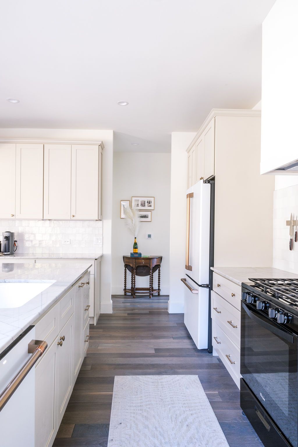 A kitchen with white cabinets , a black stove , a refrigerator , a sink , and a rug.