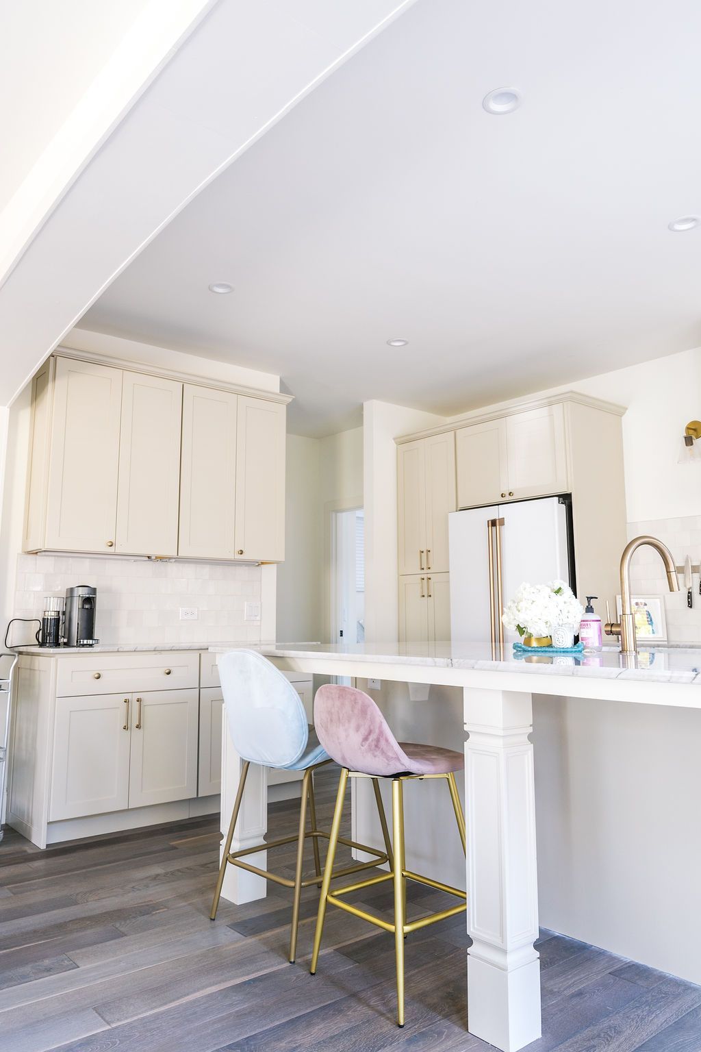 A kitchen with white cabinets , a sink , a refrigerator , and a bar.