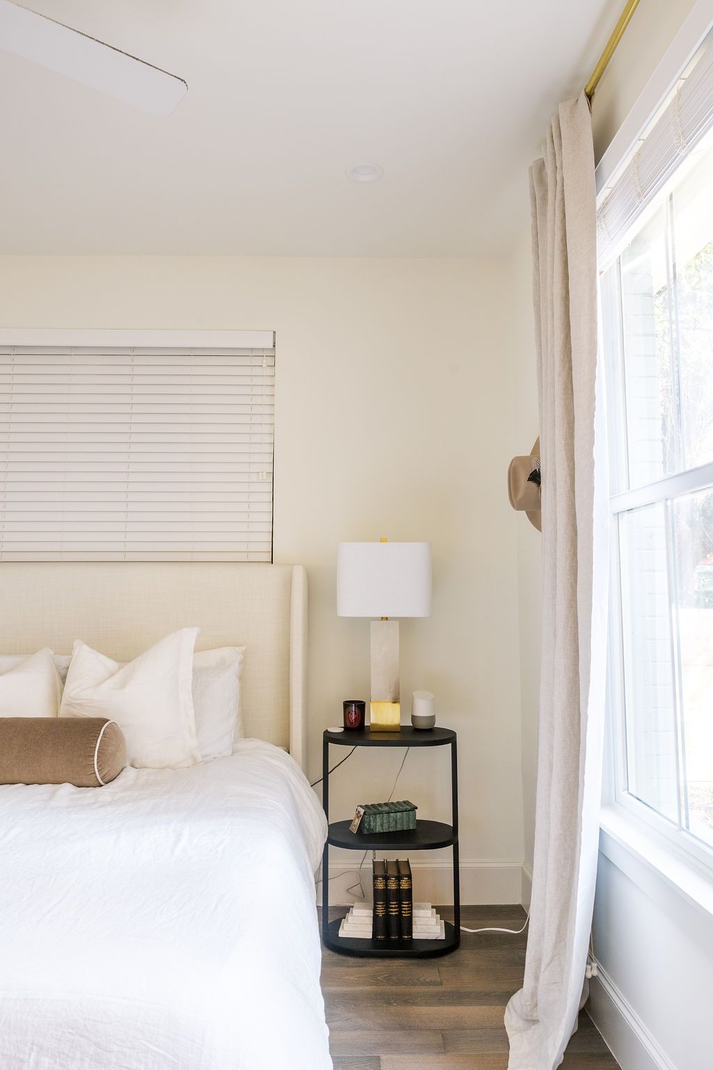 A bedroom with a bed , nightstand , lamp and window.