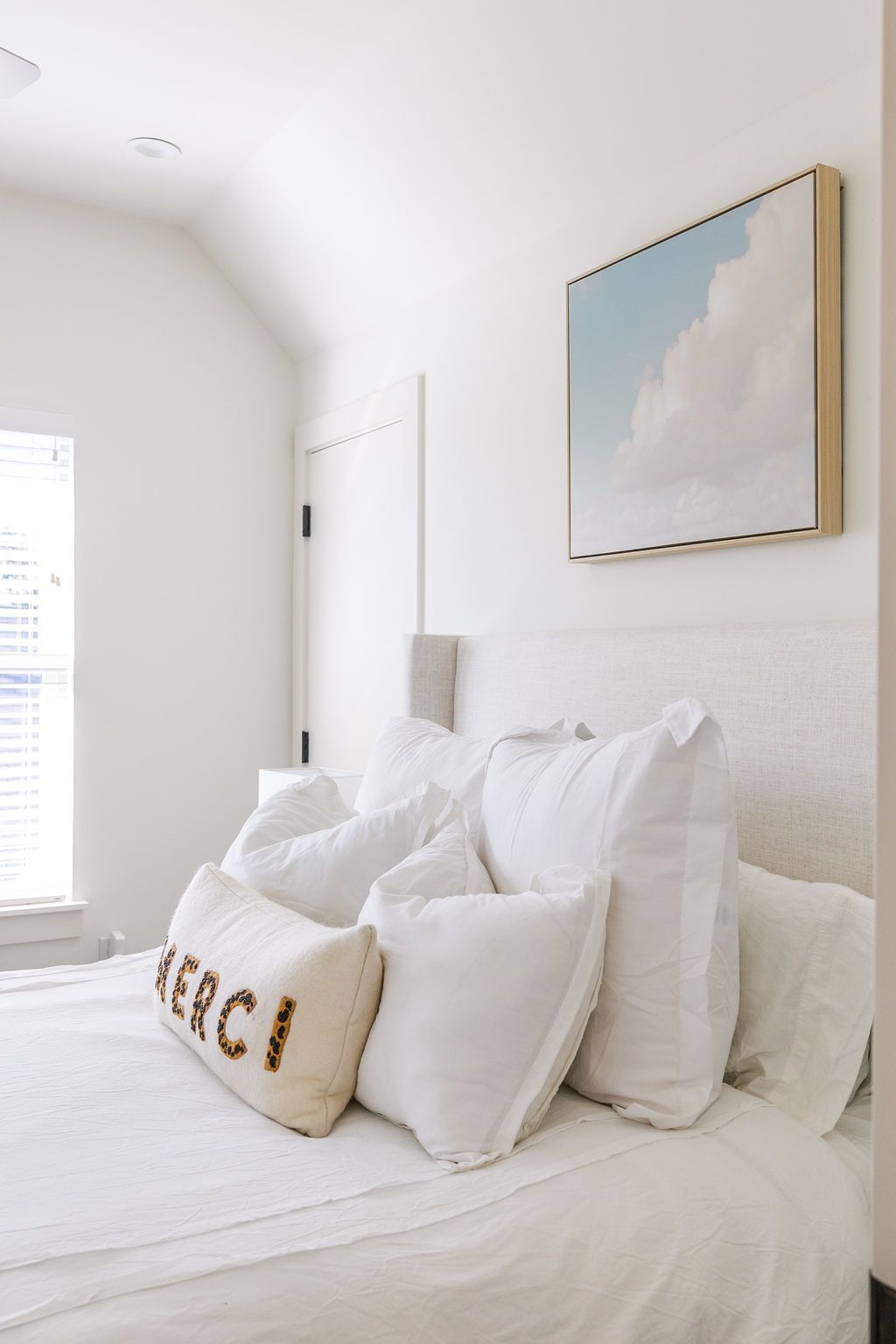 A bed with white sheets and pillows and a painting on the wall above it.
