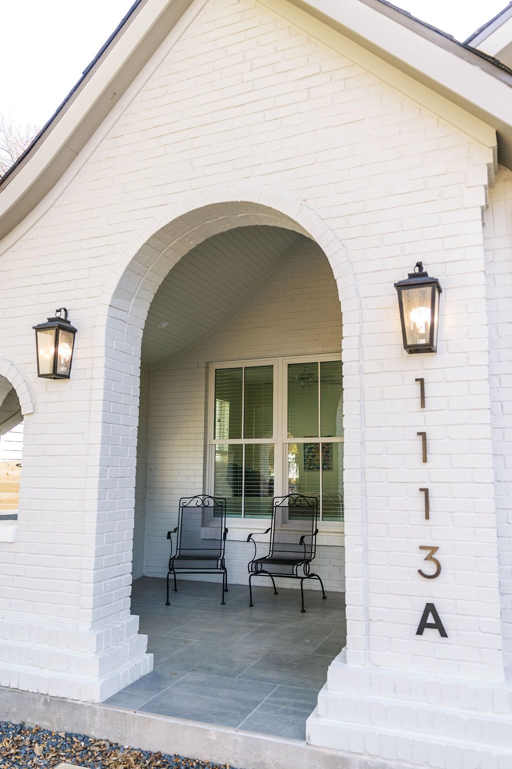 A white brick house with a porch and chairs