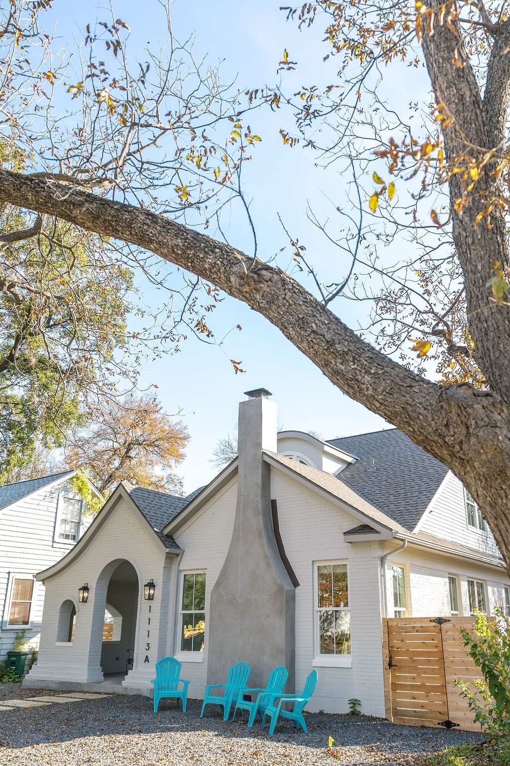 A white house with blue chairs in front of it and a tree.