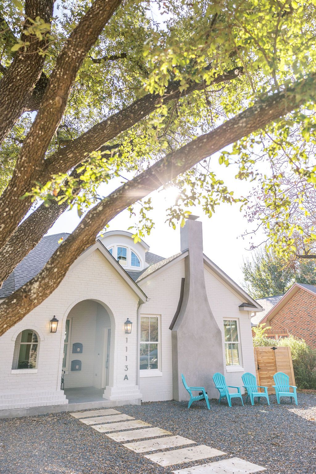 A white house with blue chairs in front of it and a tree.