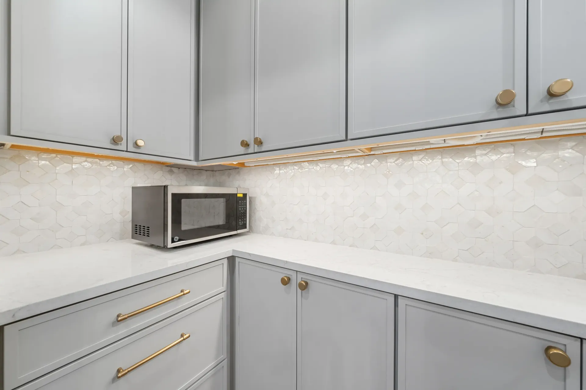 Gray kitchen cabinets with gold hardware and a microwave.