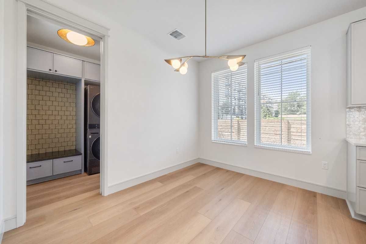 Empty dining room with wood floors, two windows, and modern light fixture. Laundry room visible on the left.