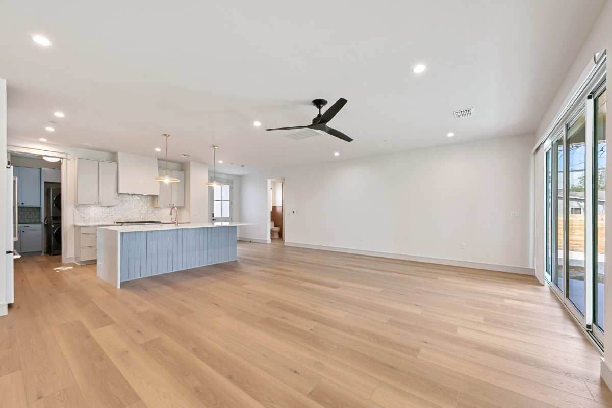 Open-concept living space with light wood floors, a blue island, and a sliding glass door.