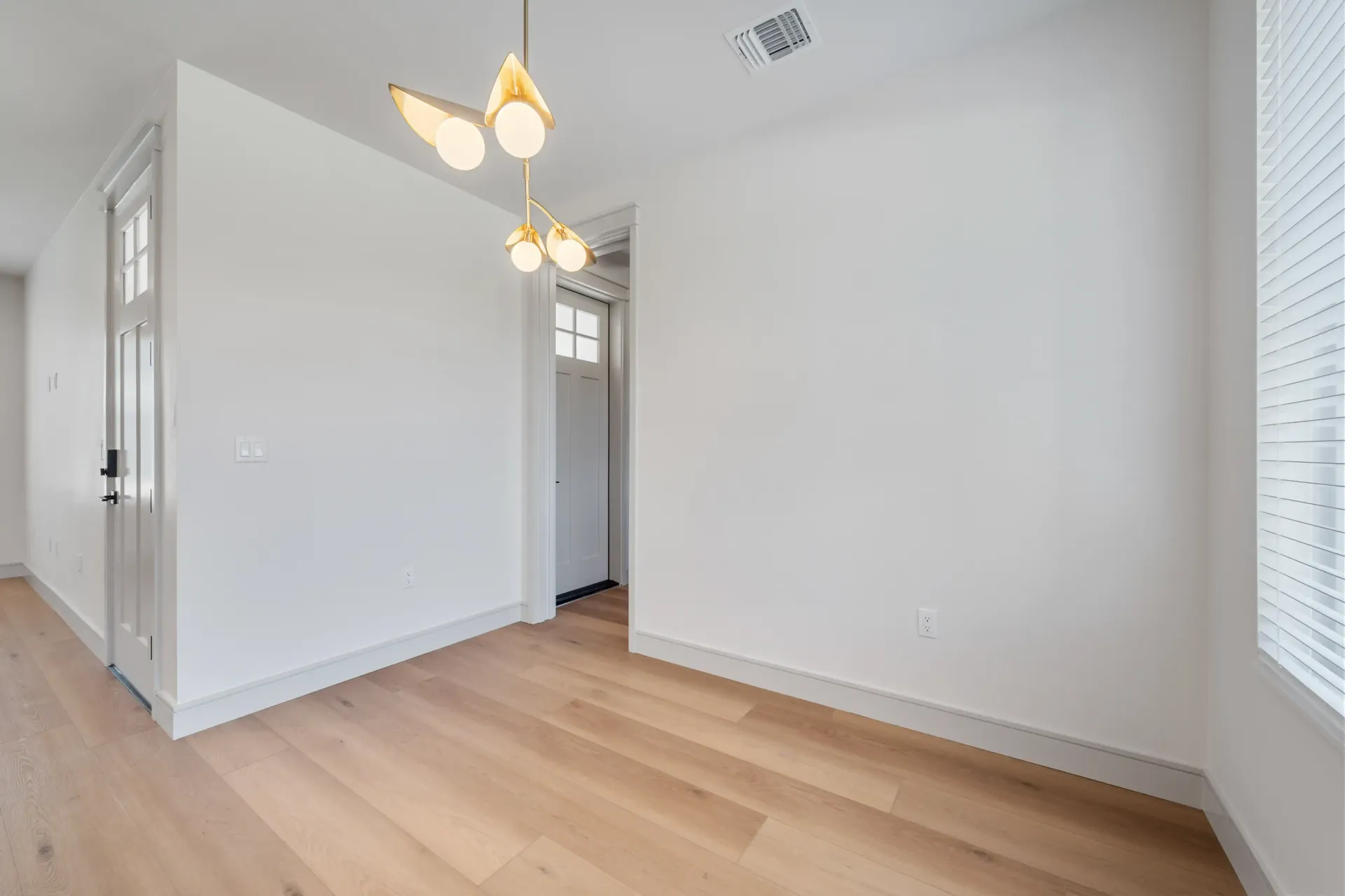 Empty room with light wood floors, white walls, and a modern gold chandelier.