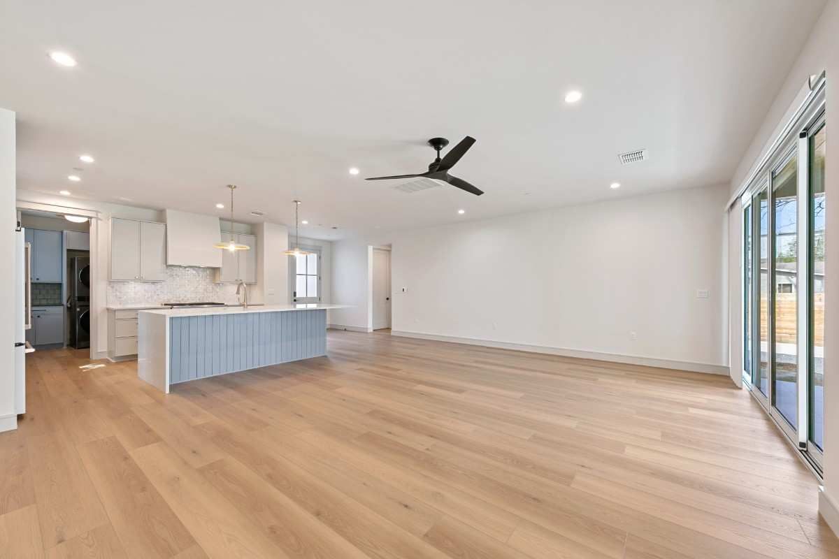 Open-concept living space with light wood floors, white walls, and a blue kitchen island. Sliding glass doors.