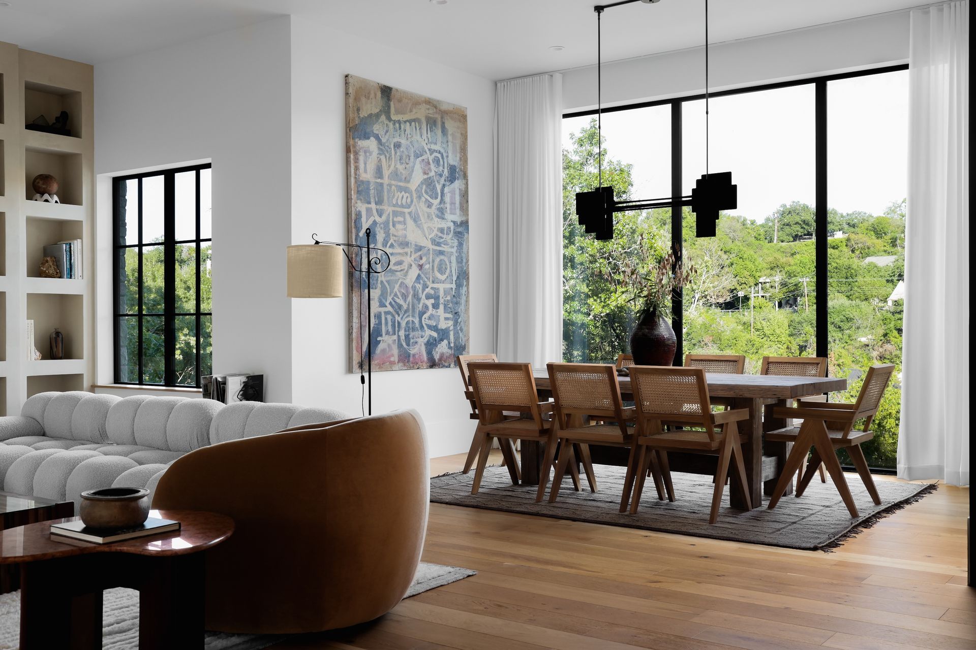 Modern dining room with a large window overlooking trees, a wooden table, and chairs.