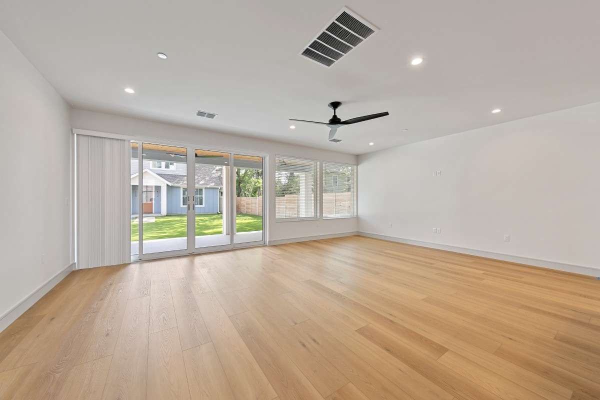 Empty room with light wood floors, white walls, large glass doors, and a ceiling fan.