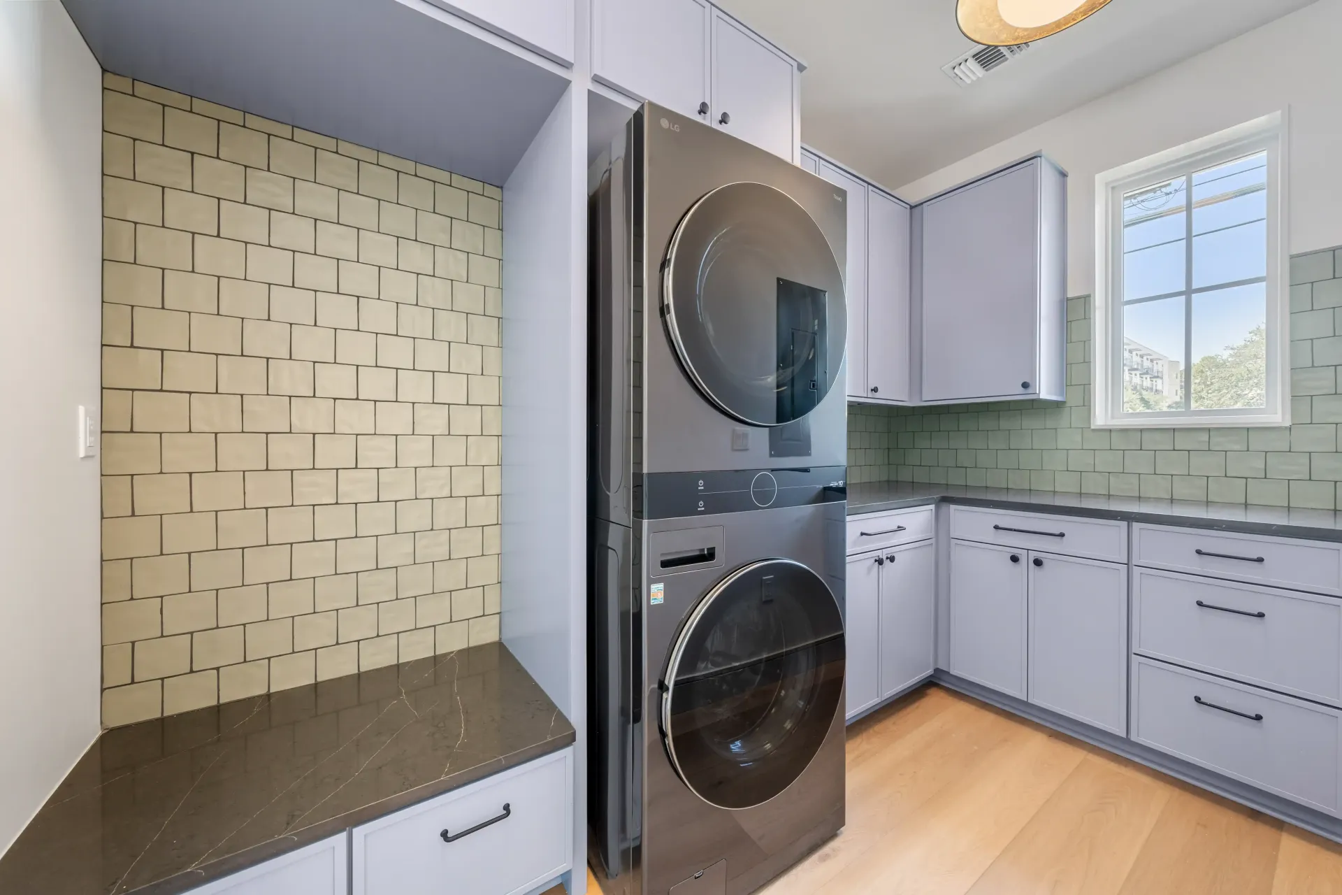 Laundry room with stacked washer/dryer, light blue cabinets, and patterned wall tile.