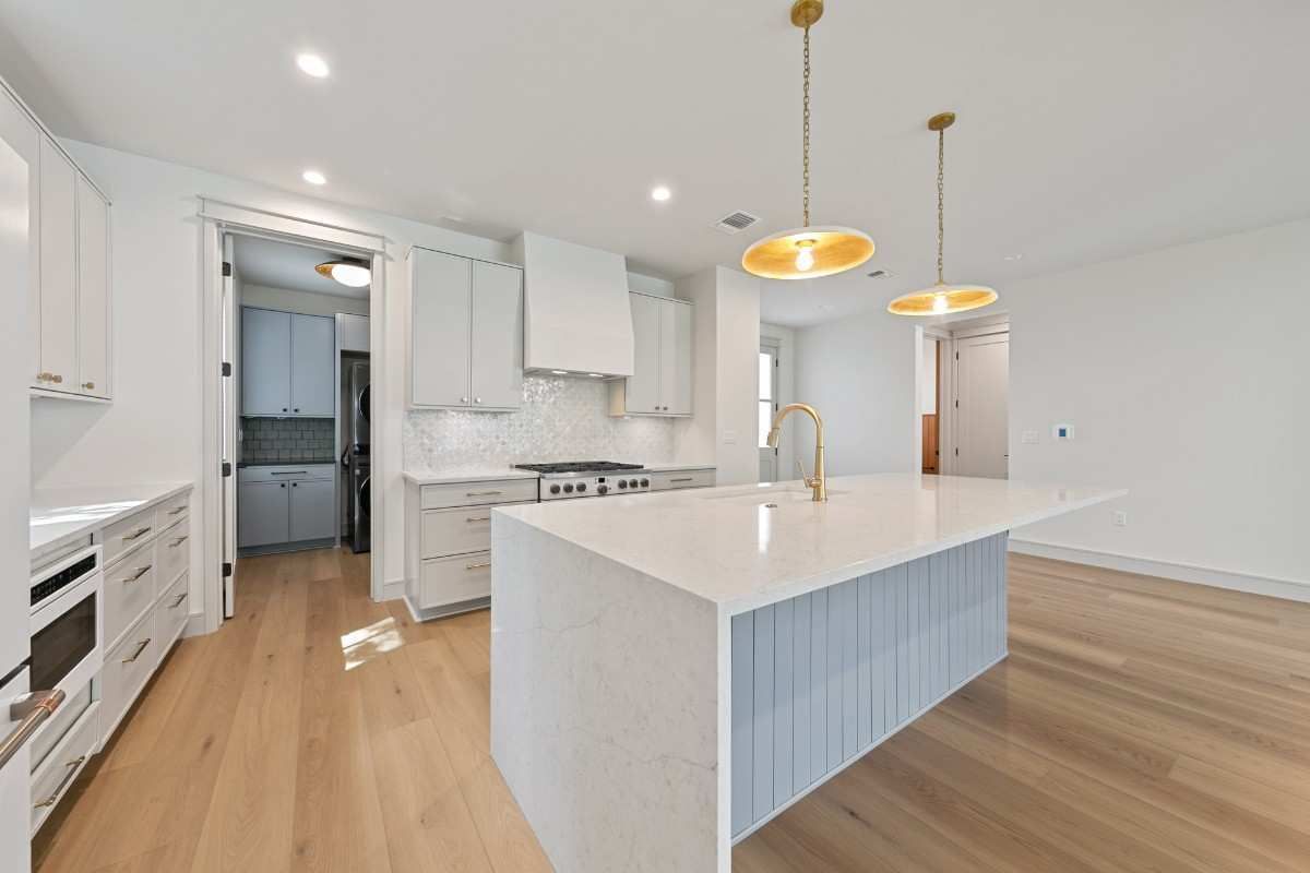 Spacious white kitchen with light wood floors, a large island, and gold pendant lights.