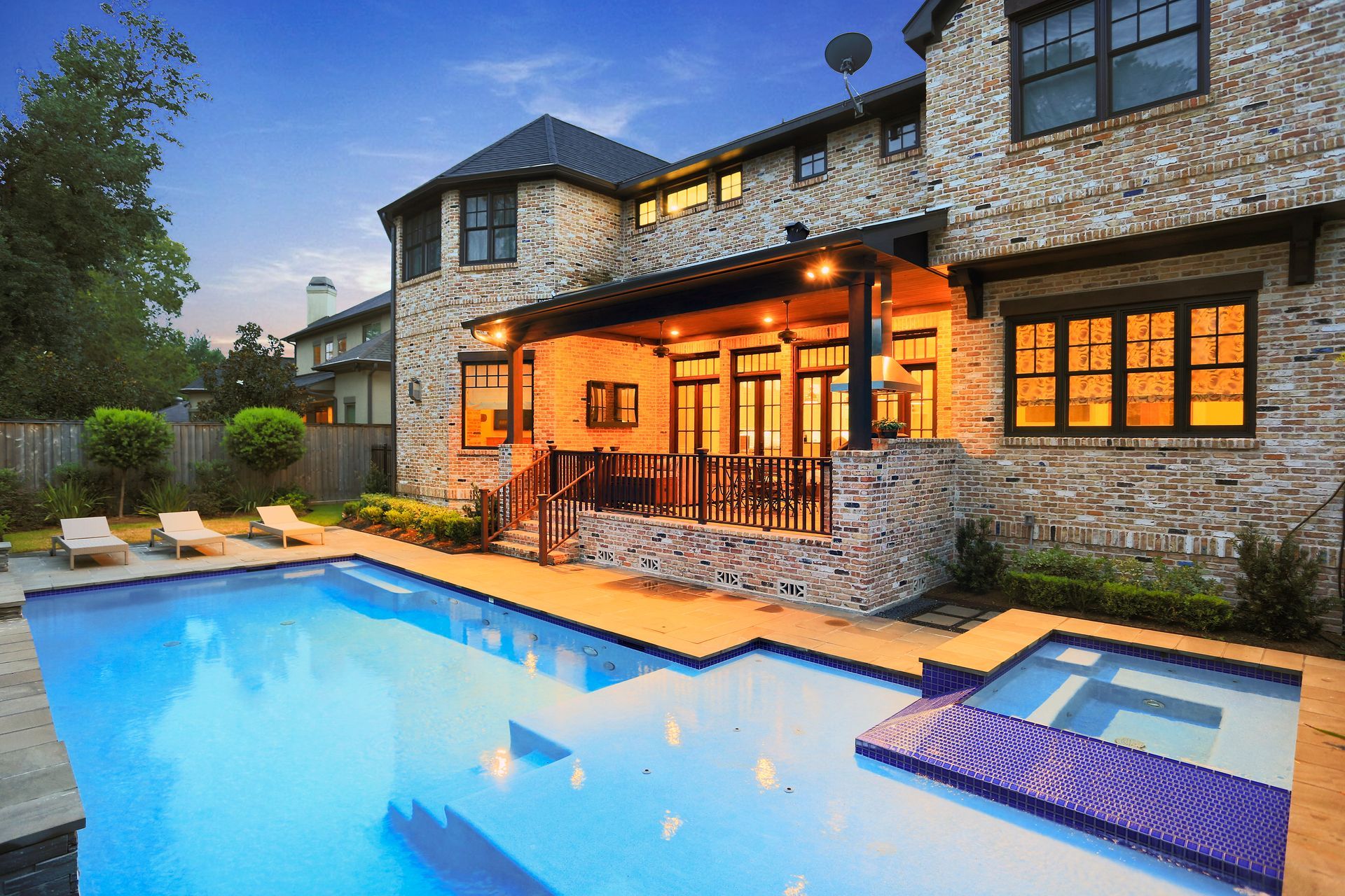 Luxury home exterior with pool and spa, stone and brick construction, lit patio, blue water.