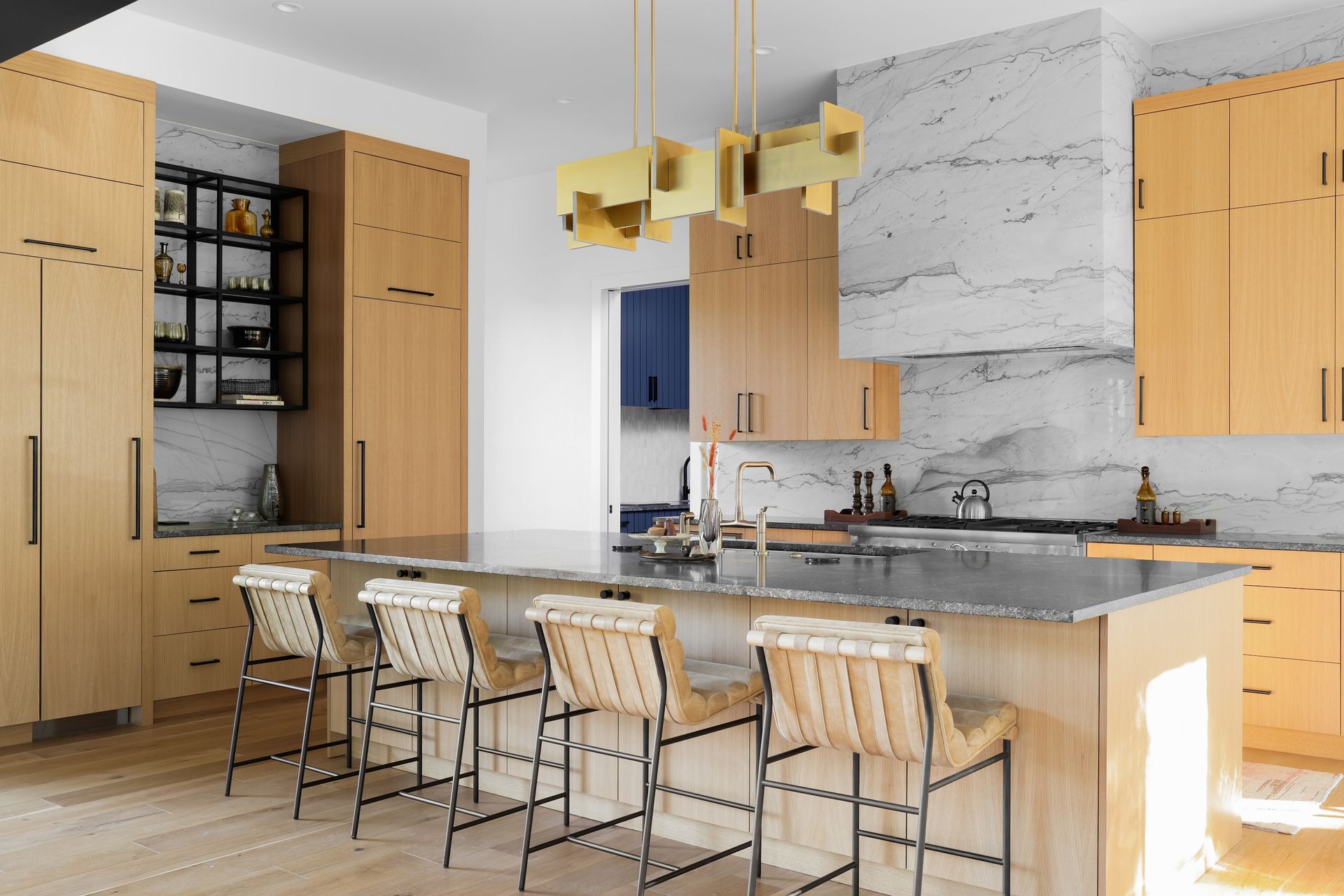 Modern kitchen with light wood cabinetry, marble backsplash, island with seating, and gold pendant light.