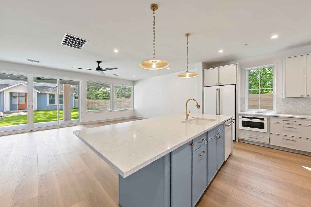 Modern kitchen with island, white cabinetry, light blue base, wood floors, and backyard view.