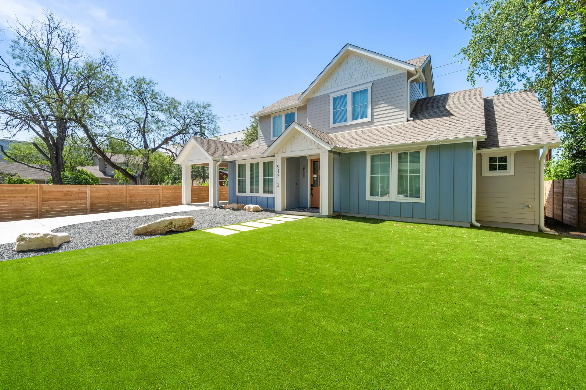 Blue and gray two-story house with green lawn and bright blue sky.