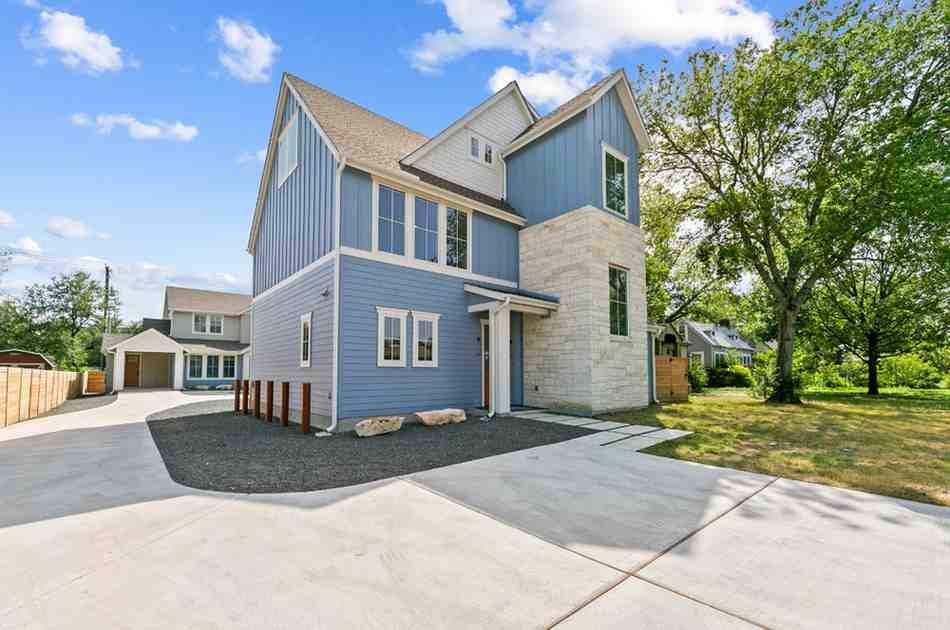 Modern two-story house with blue siding and stone accents, driveway, and detached garage on a sunny day.