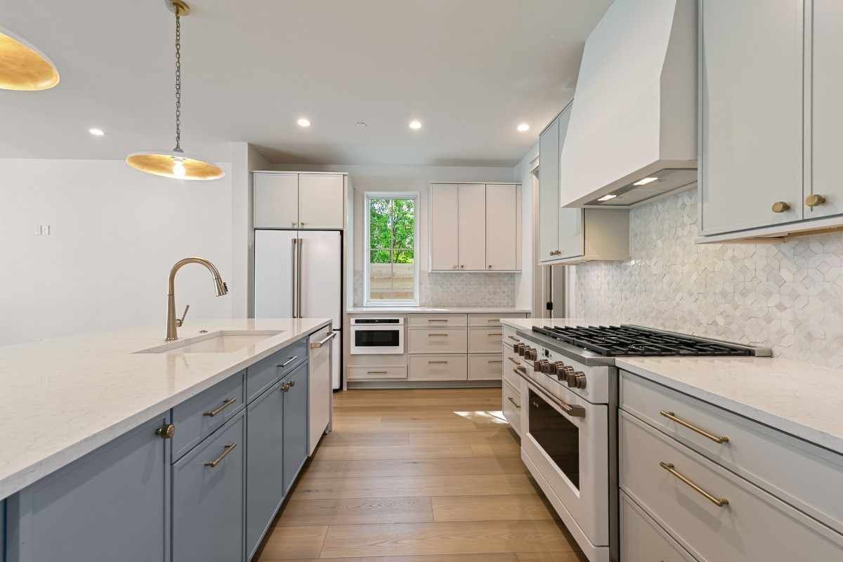 Modern kitchen with a long island and stainless steel appliances; light blue and white cabinetry, gold fixtures.