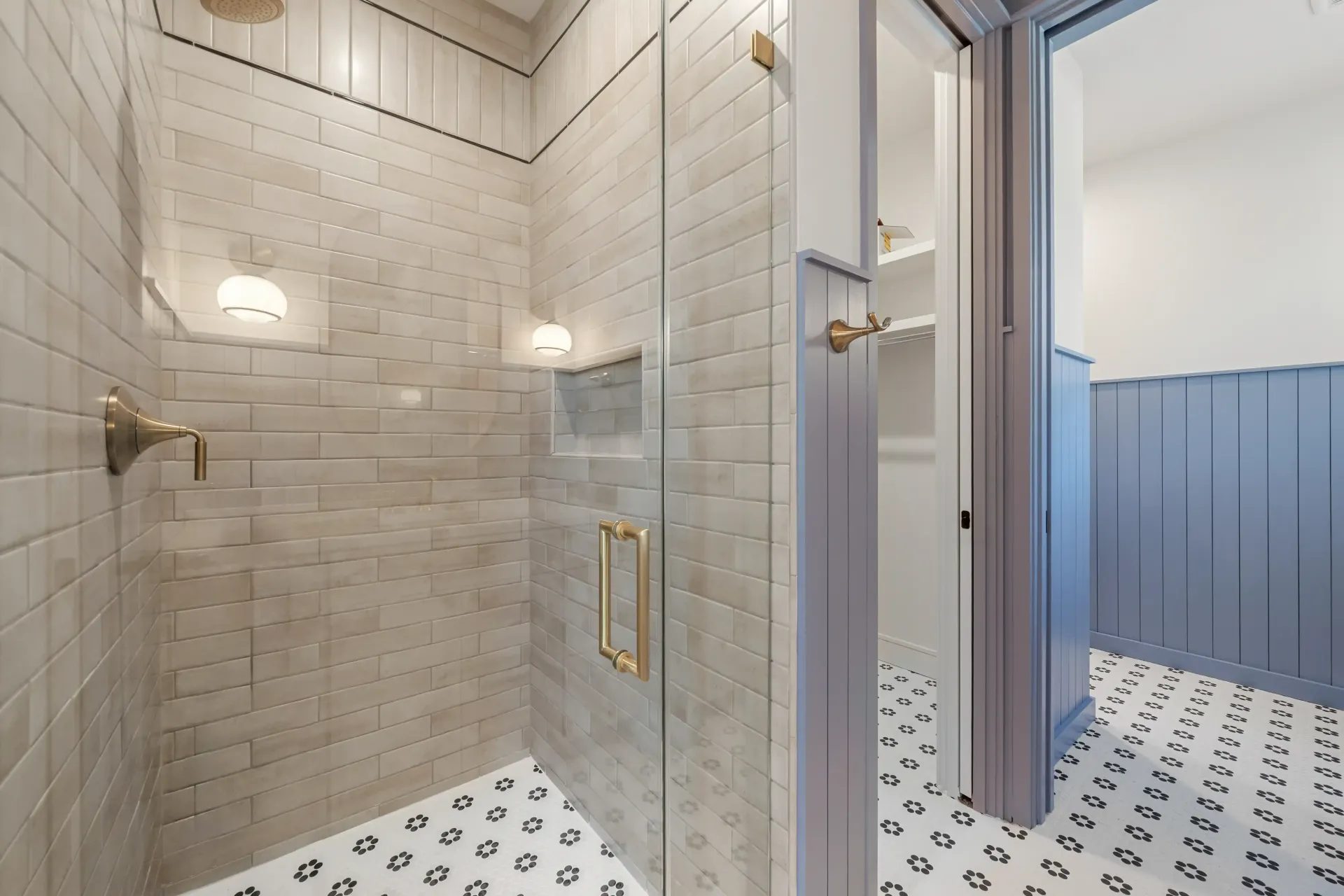 Shower with glass door, tiled walls, and patterned floor. Open door to a closet.