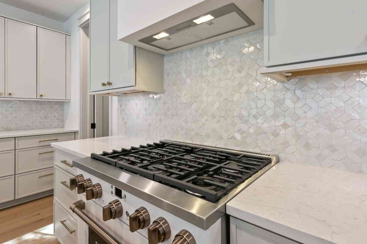 Kitchen with white cabinets, stove, range hood, and patterned backsplash.