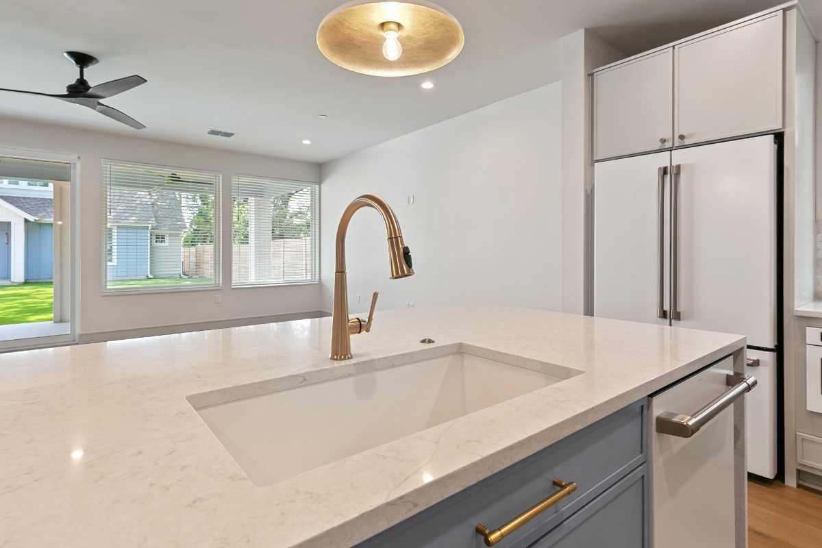 Modern kitchen with white countertop island, gold faucet, and large windows.