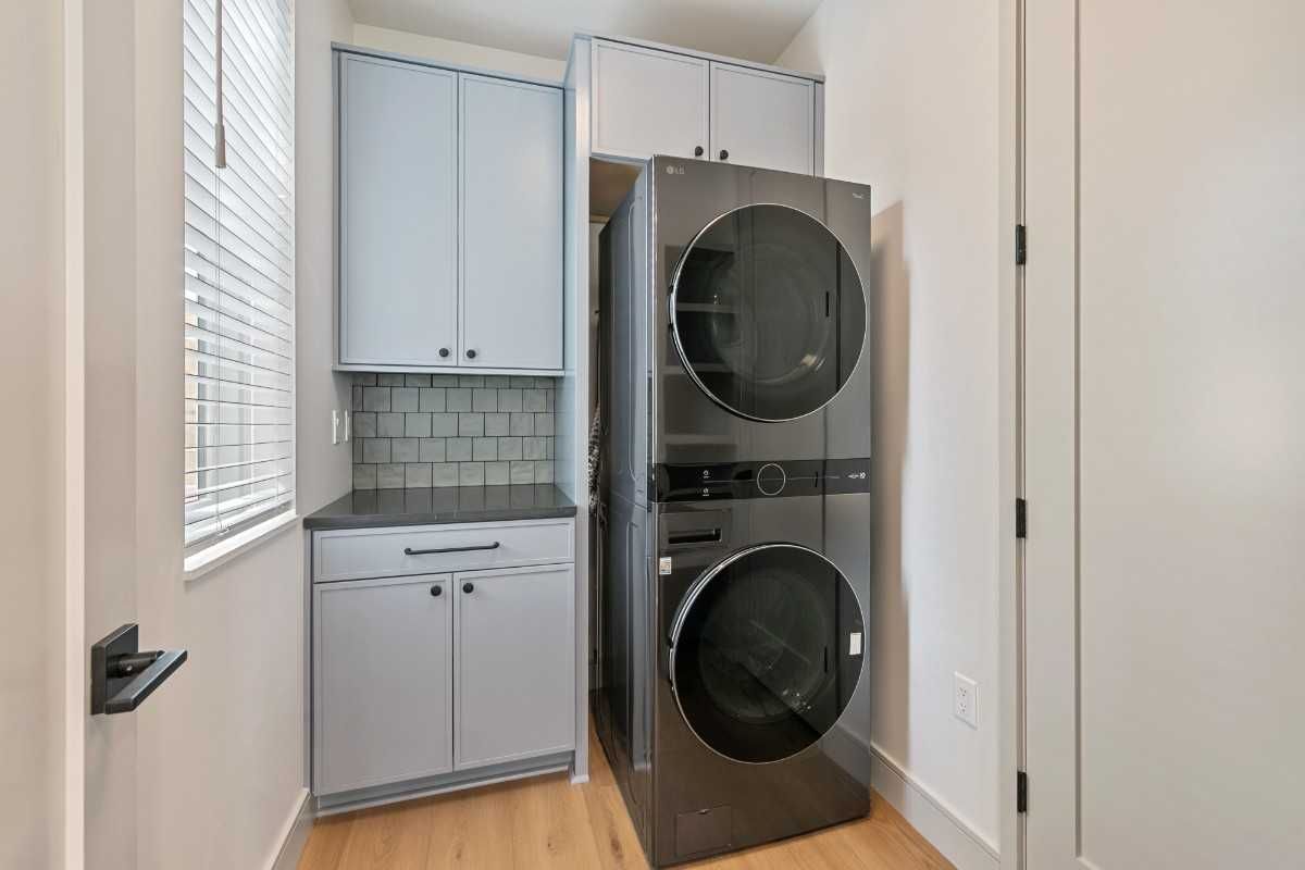 Laundry room with stacked washer/dryer, grey cabinets, and a window.