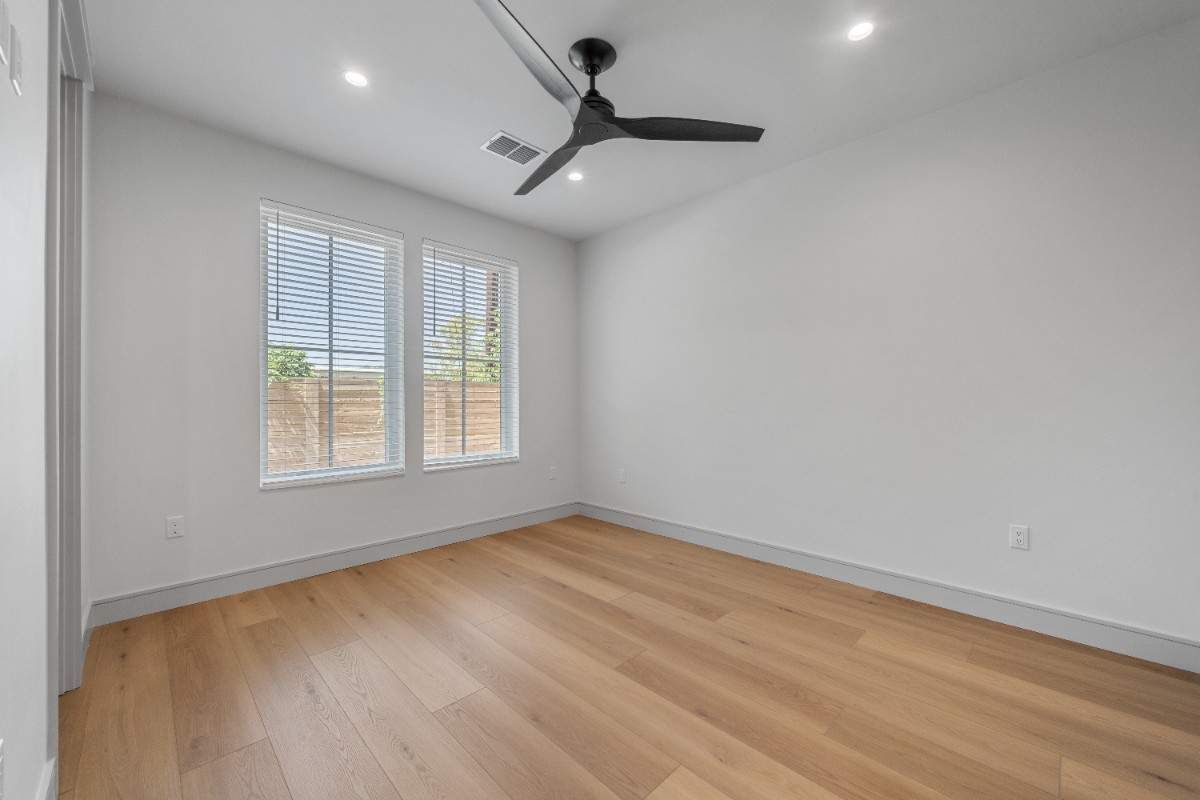 Empty room with light wood floors, white walls, two windows with blinds, and a ceiling fan.