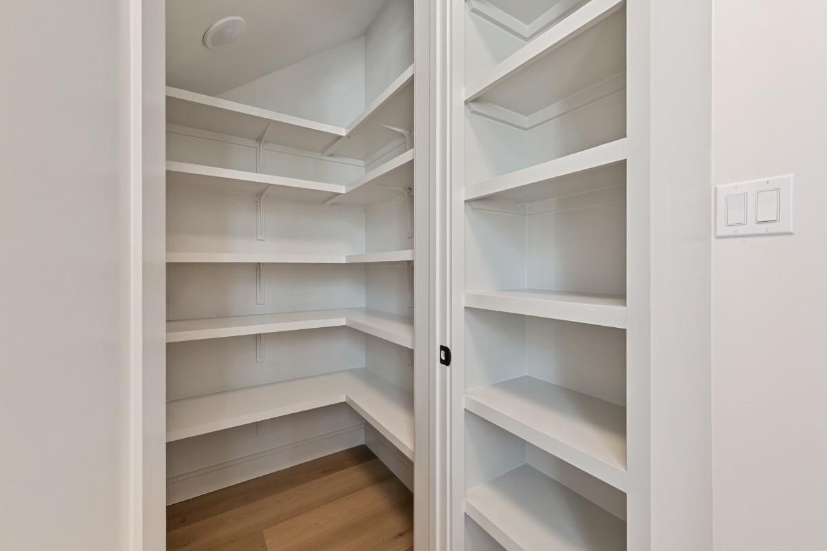 Empty white pantry with multiple shelves. Wooden floor. Doorway to right.