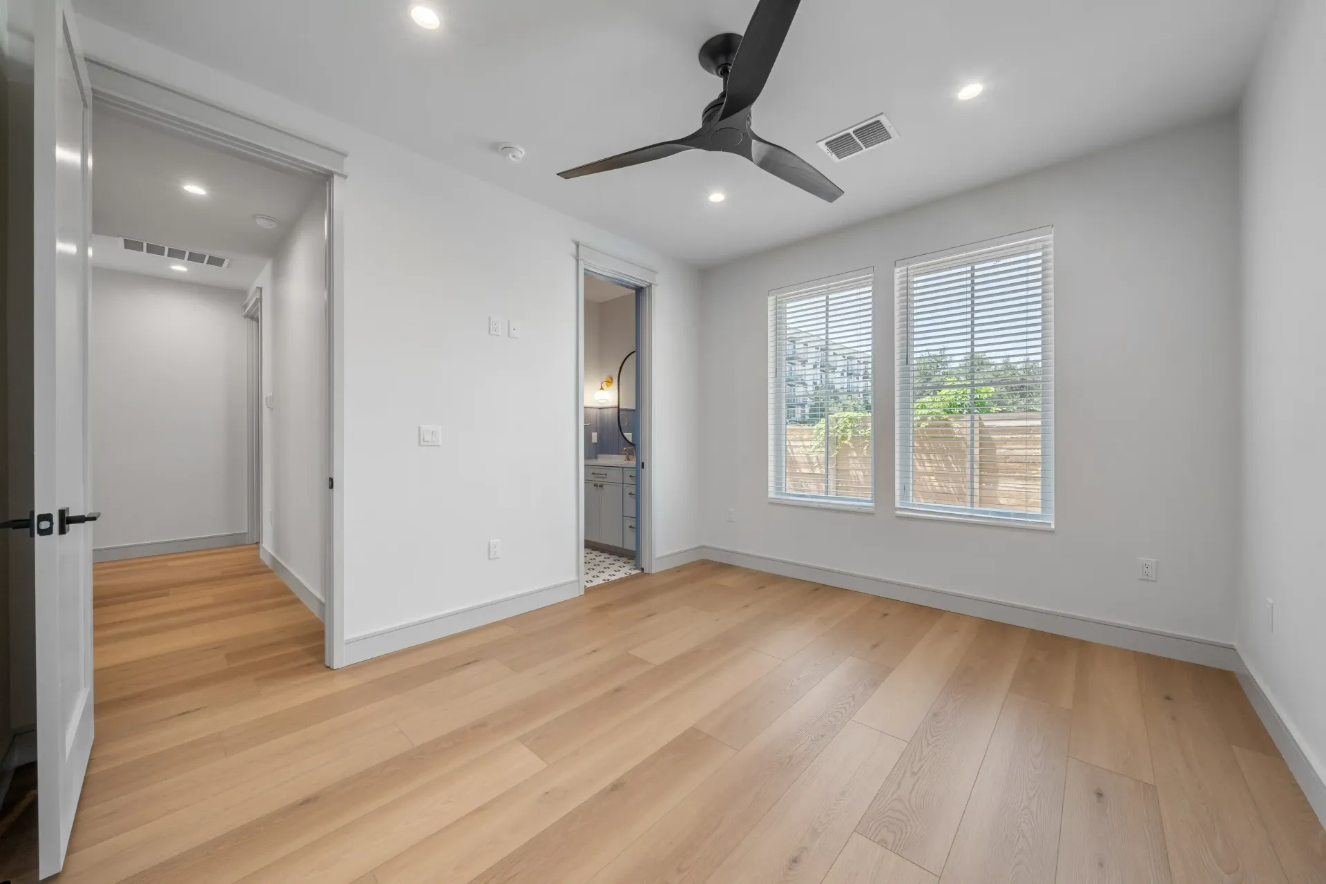 Empty room with hardwood floors, a ceiling fan, and a doorway to a hallway and a bathroom.