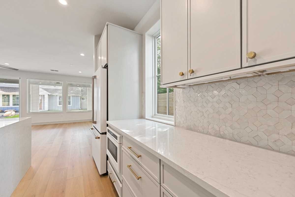 White kitchen with cabinets, countertops, and appliances; a window and wood flooring.